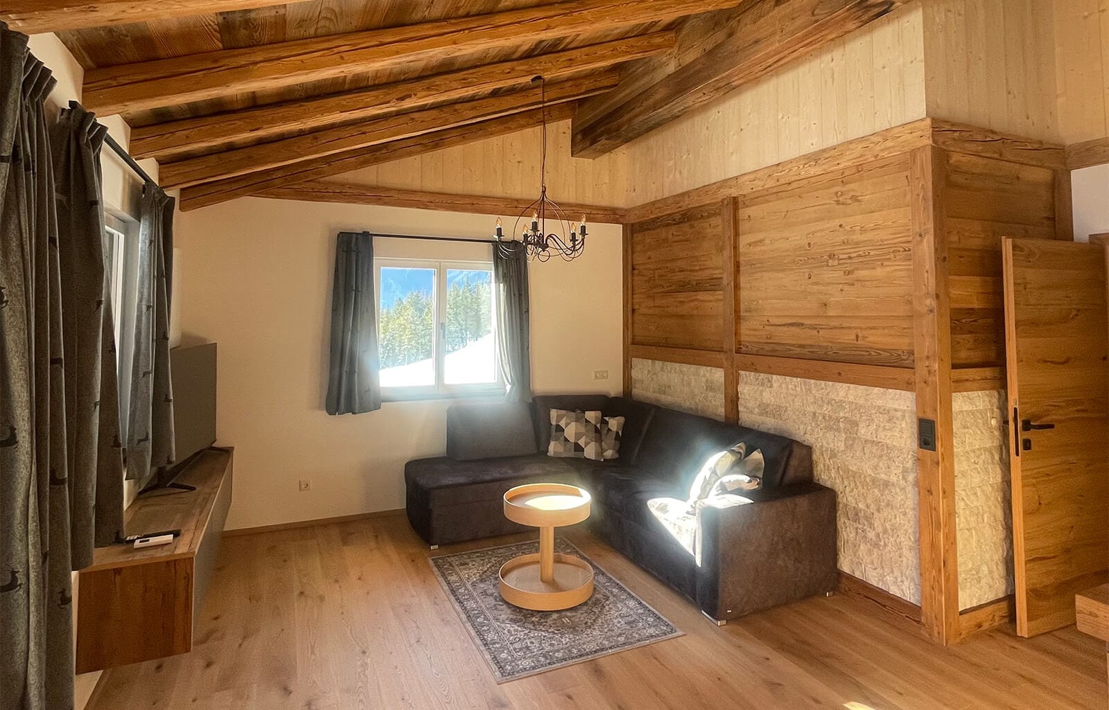 Gemütlicher Wohnbereich im Apartment Bischofsmütze mit bequemer Couch, modernen Holzpaneelen und warmem Lichtdesign für entspannte Urlaubsstunden.