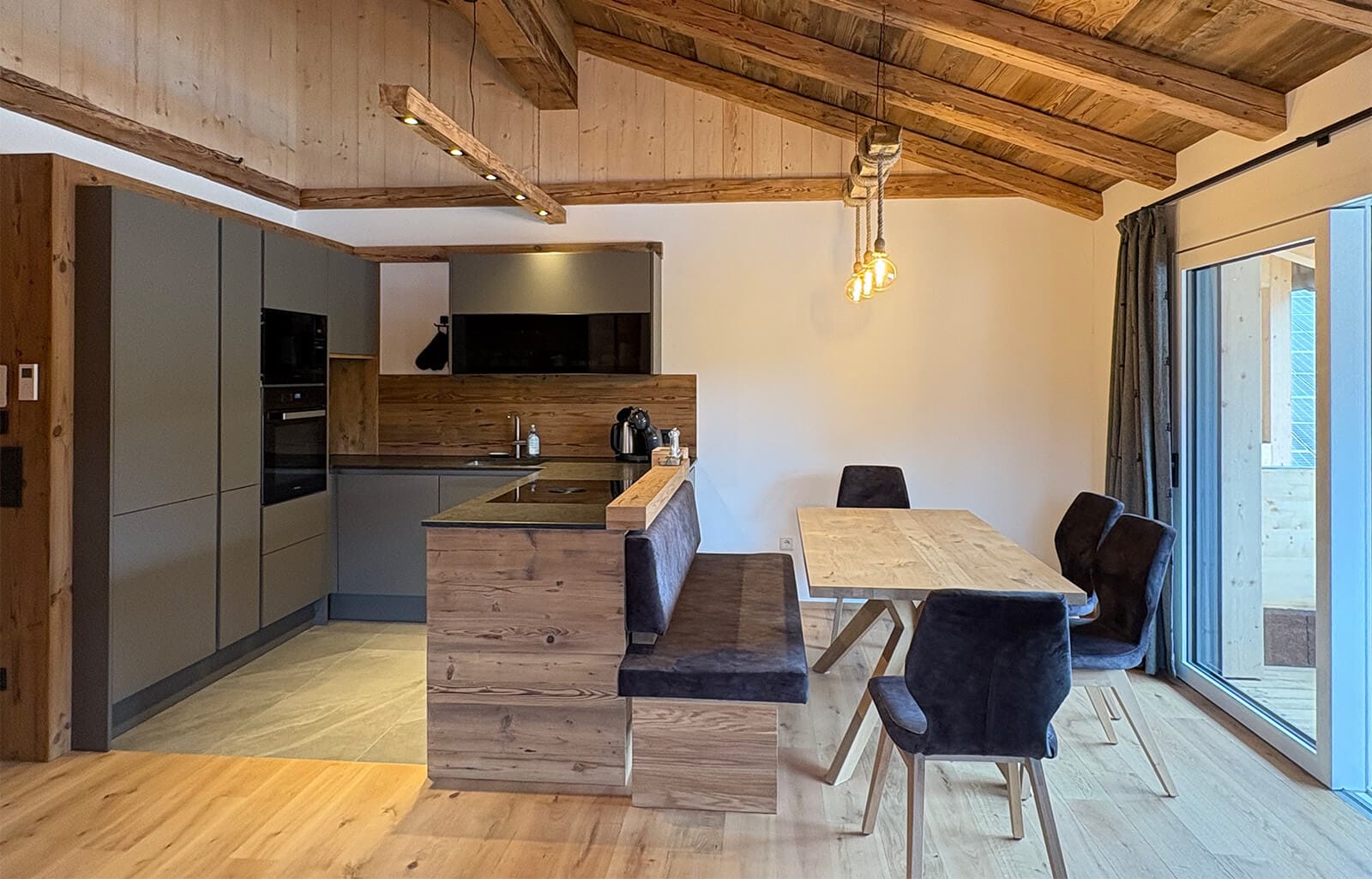 Offener Wohn-Essbereich im Apartment Bischofsmütze mit moderner, voll ausgestatteter Küche, massivem Esstisch und großen Panoramafenstern für ein helles Wohnambiente.