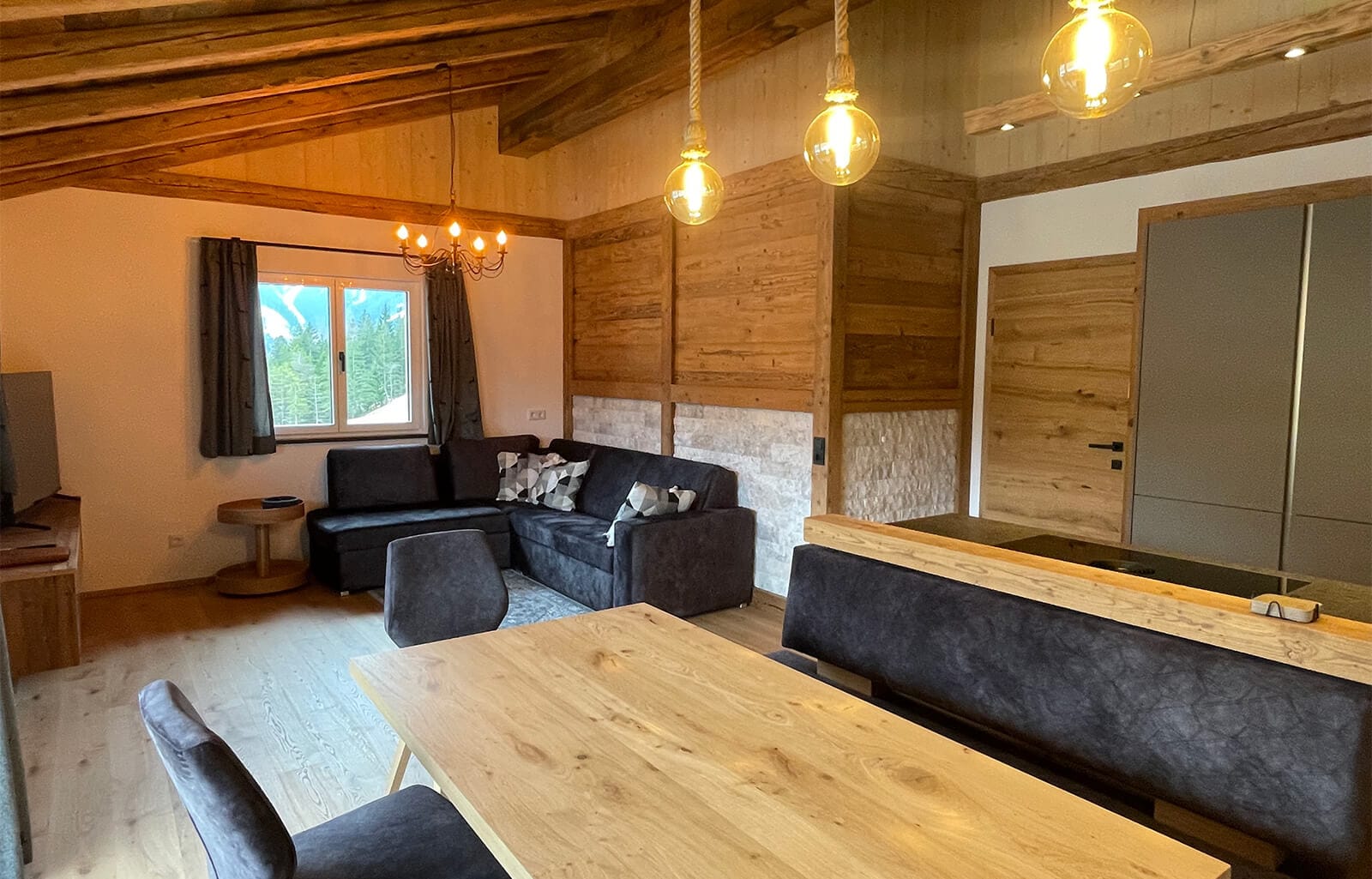 Lichtdurchfluteter, offener Wohn- und Essbereich im Apartment Bischofsmütze mit moderner Eckküche, großzügiger Tafel und gemütlicher Sitzecke in alpinem Design.
